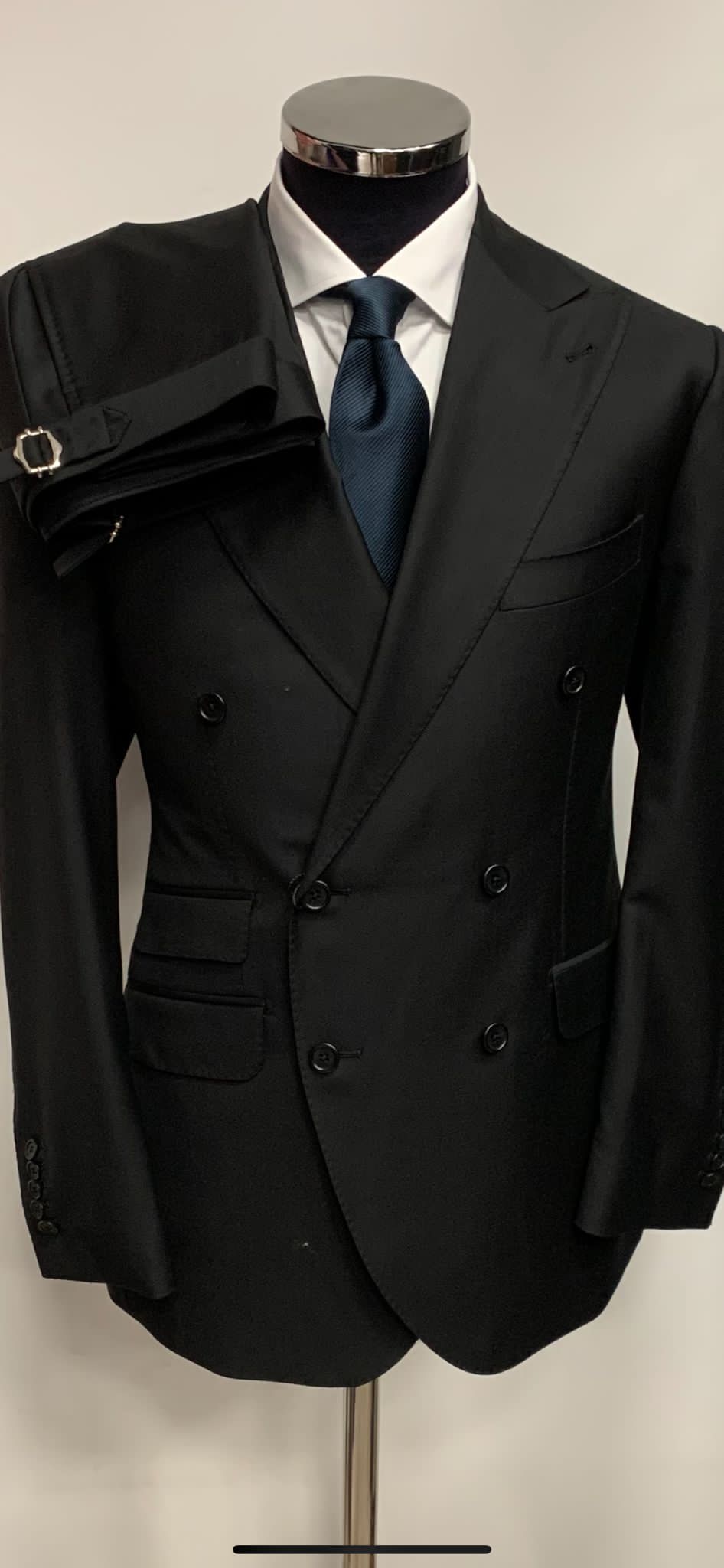 Black super 150 Cerruti wool Neapolitan double breasted wool suit. Ticket pocket, 5 inch peak lapel, hand stitched, double vent, soft Neapolitan shoulders, side buckle on flat front pant. Available in size 38-60 Regular or Long.